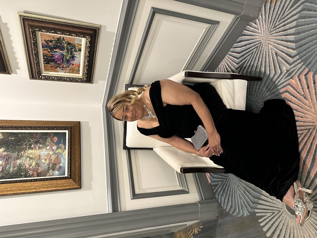 A woman in a black dress seated in an elegant room.